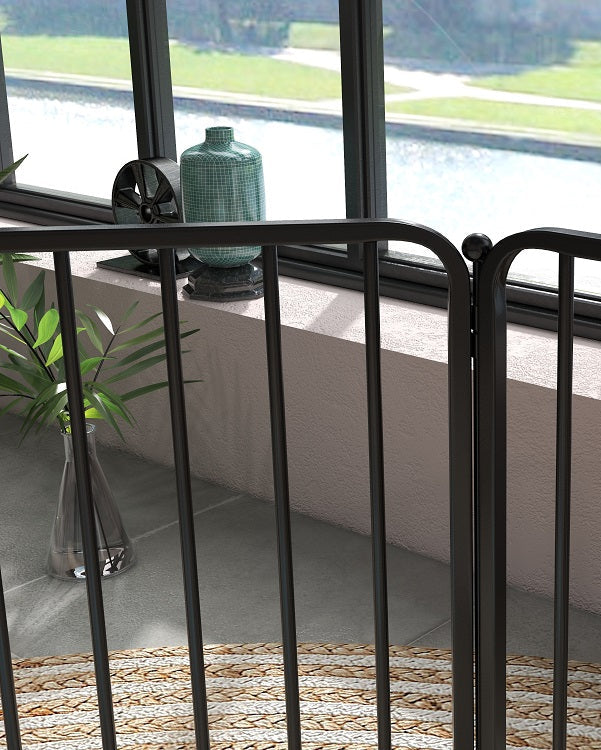 Black metal gate in a room with large windows showing a garden view.